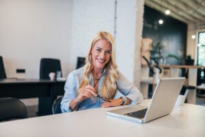 beautiful-blonde-woman-workplace-holding-eyeglasses-looking-camera - SIM Computer Laptop to narzędzie pracy, nauki czy rozrywki dla wielu z nas. Wybierając idealny sprzęt, zwracamy uwagę na różne aspekty - wydajność, design, funkcjonalność oraz cenę